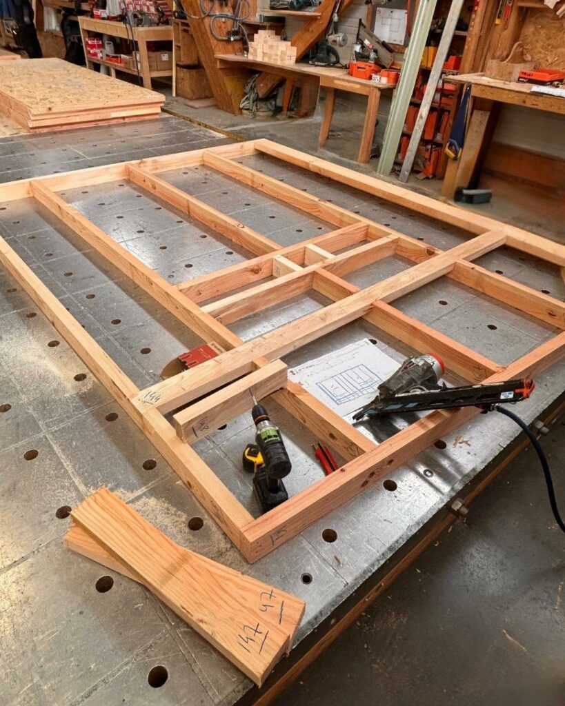 Élément d’ossature bois en cours d’assemblage sur une table de travail dans un atelier, avec outils et plans de construction posés à proximité.